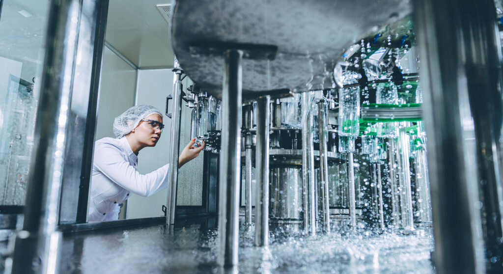 photograph of woman checking filling machine in pet water bottling facility